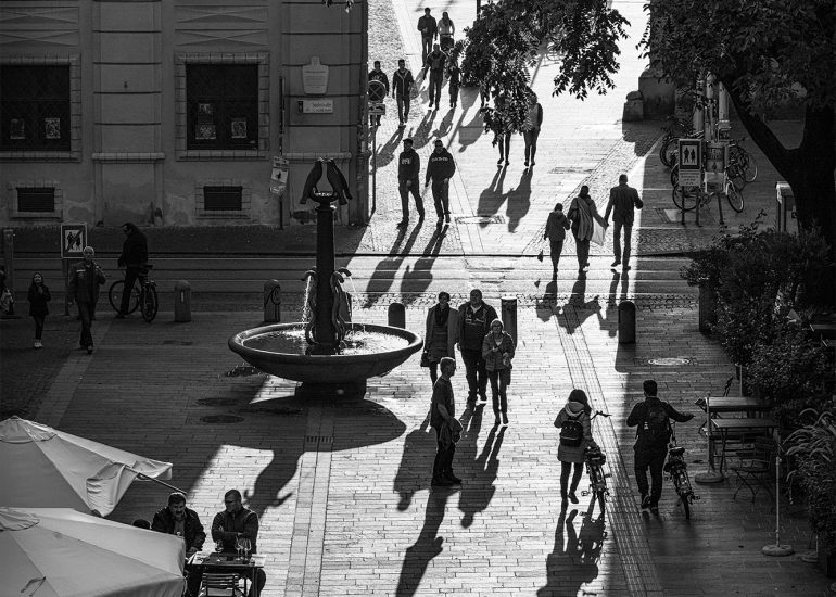 Schloßbergplatz in Graz kurz vor Sonnenuntergang. Ein Breiter Lichtstreifen verläuft quer über den Platz während der Rest sich im Schatten befindet.